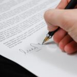 a white hand signing a contract with a pen